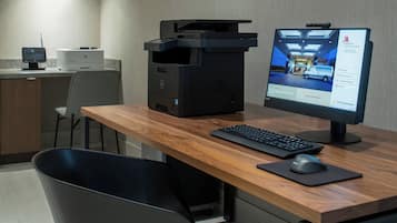 Habitación de hotel con escritorio, ordenador de sobremesa, impresora y monitor mostrando el interior de un hotel.