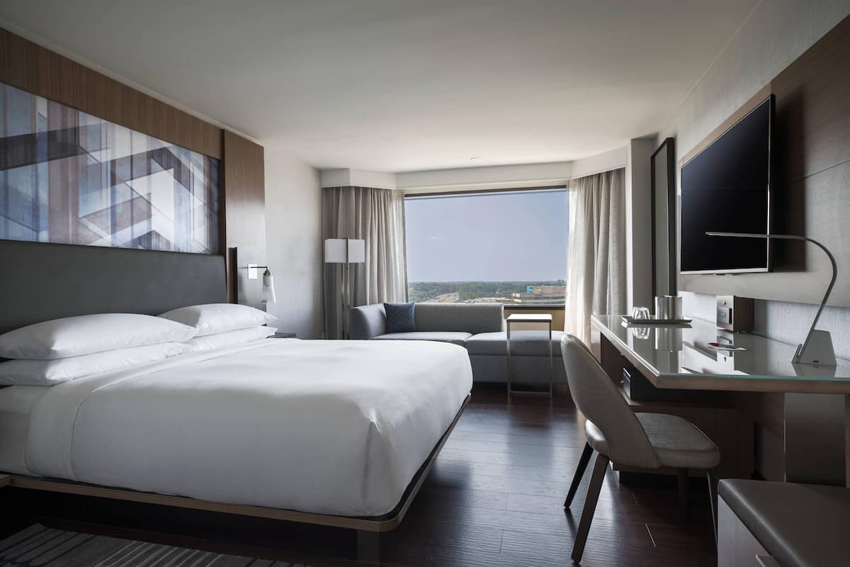 A modern hotel room with a large bed, a desk, a chair, and a TV.