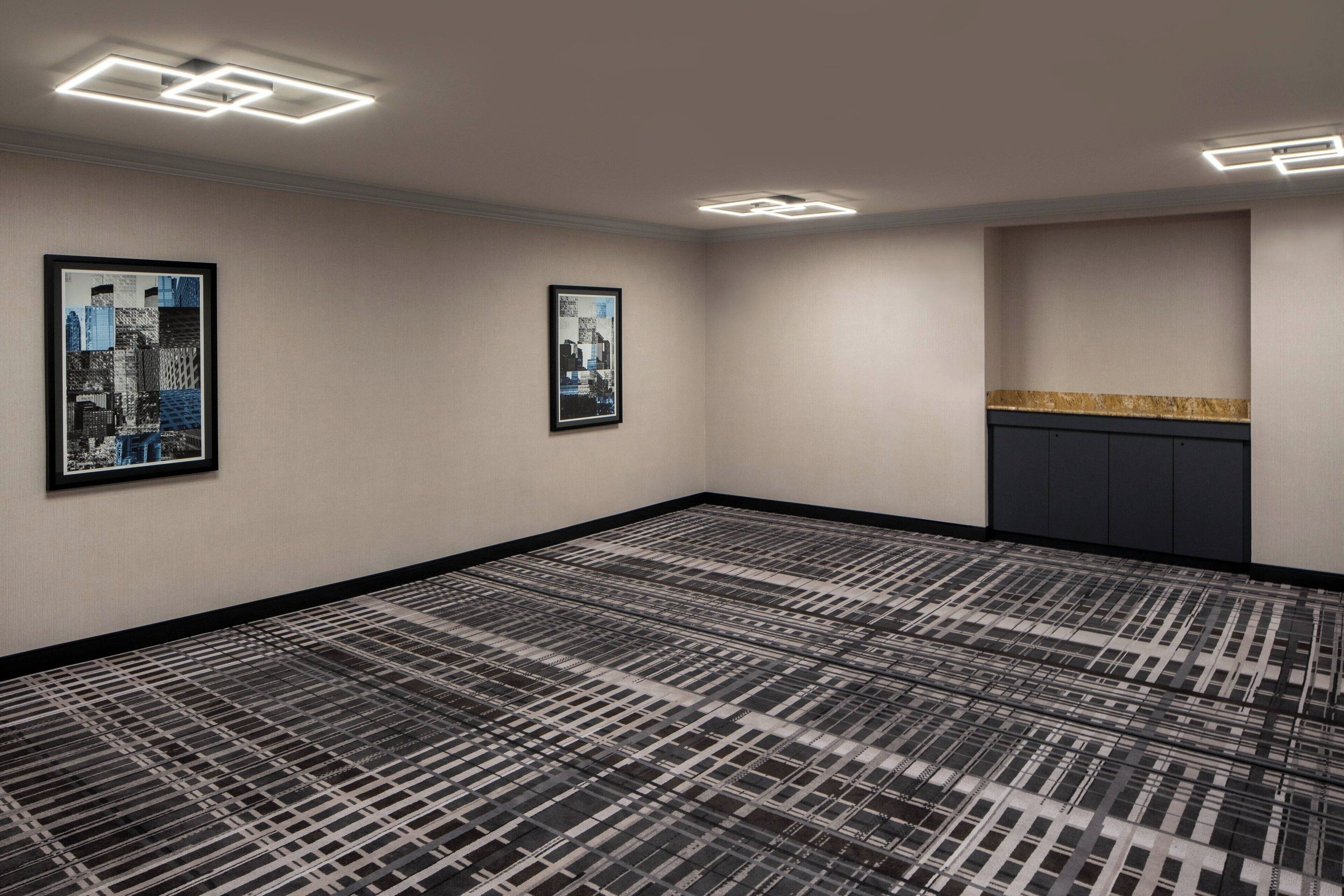 A hotel room with a patterned carpet, two framed pictures on the wall, and a built-in cabinet with a decorative countertop.