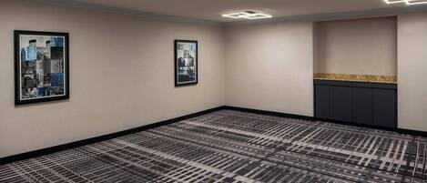 A hotel room with a patterned carpet, two framed pictures on the wall, and a built-in cabinet with a decorative countertop.