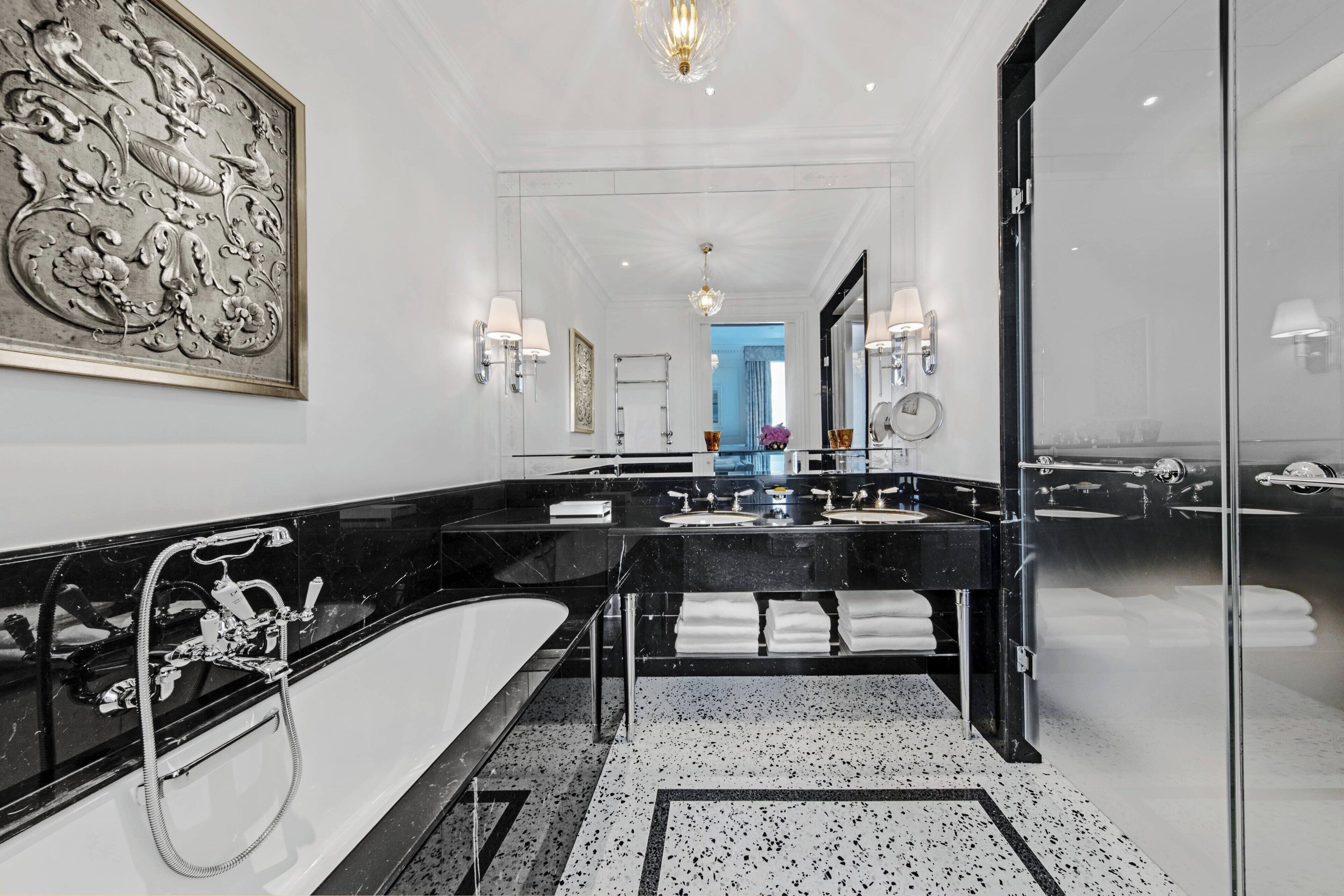 A modern bathroom with a large mirror, two sinks, a bathtub, and a decorative wall piece.