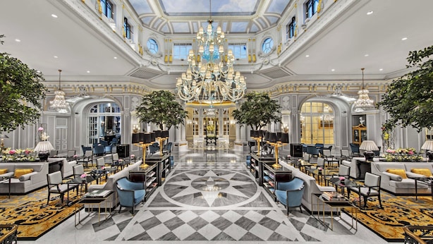 A grand lobby with a large chandelier, symmetrical seating, and a central floral arrangement.