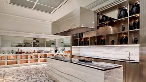 A modern kitchen with marble countertops, a central island, and a display of black vases on shelves.