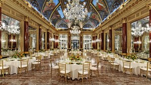 Un salón de banquetes amplio con varias mesas redondas, candelabros ornamentales y un fresco en el techo.