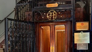 A wooden double door with a metal gate, a chandelier, and a sign with the text "VIA TATUMARE".