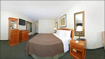 A hotel room with a large bed, a wooden dresser, a television, and a mirror.