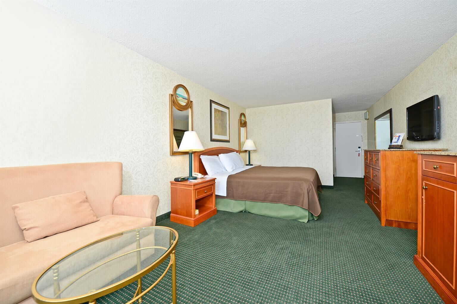 A hotel room with a bed, a sofa, a desk with a lamp, a dresser, a television, and a mirror.
