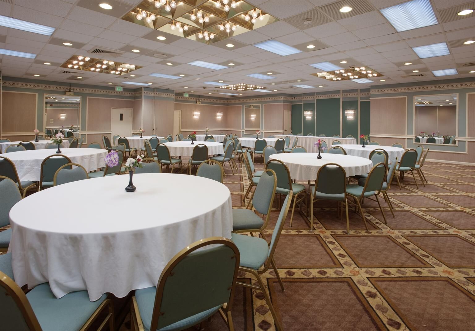 A large conference room with round tables and chairs, a patterned carpet, and a ceiling with recessed lighting.