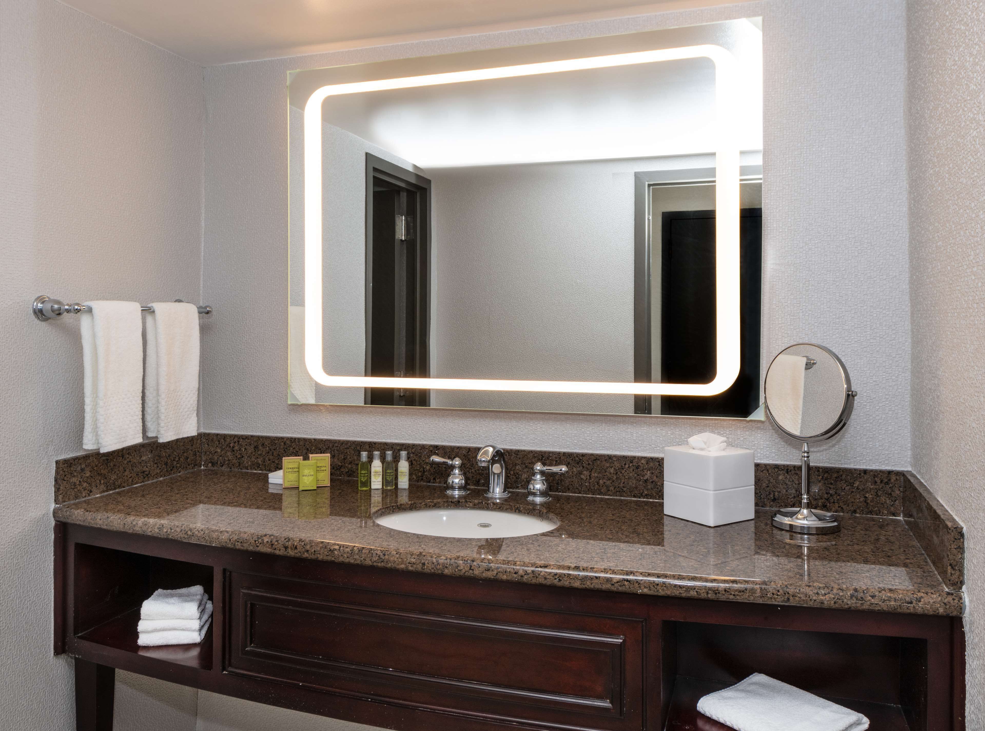 A bathroom with a granite countertop, a sink, a mirror, and a vanity with a towel rack.
