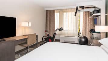 Habitación de hotel con cama, escritorio con televisor, silla, bicicleta estática y cinta de correr.