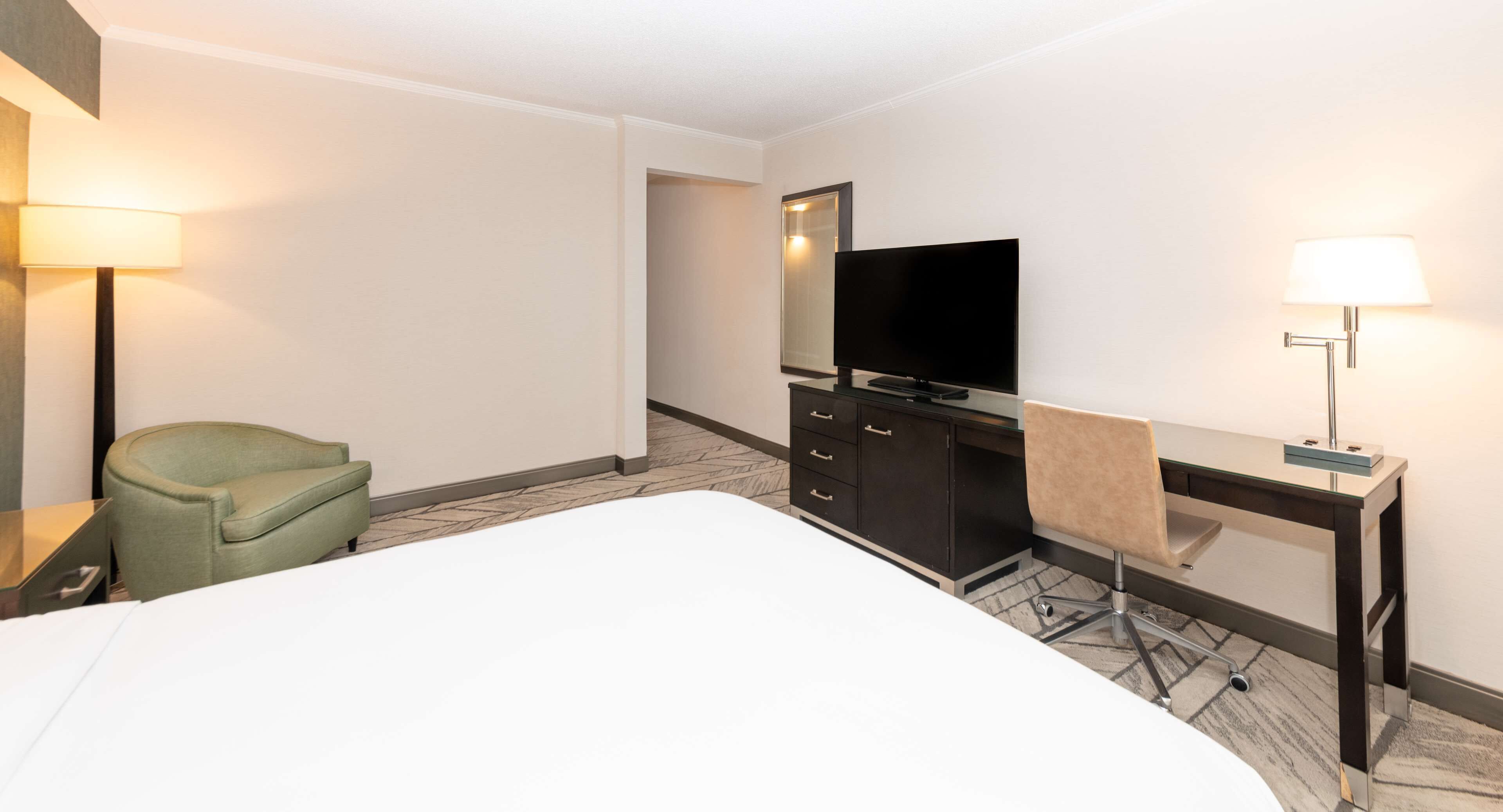Una camera d'albergo con un letto, una scrivania con una sedia, una televisione, una lampada e un armadio.