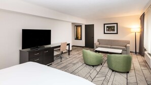 Una habitación de hotel con una cama, televisión, escritorio, sofá y dos sillones.