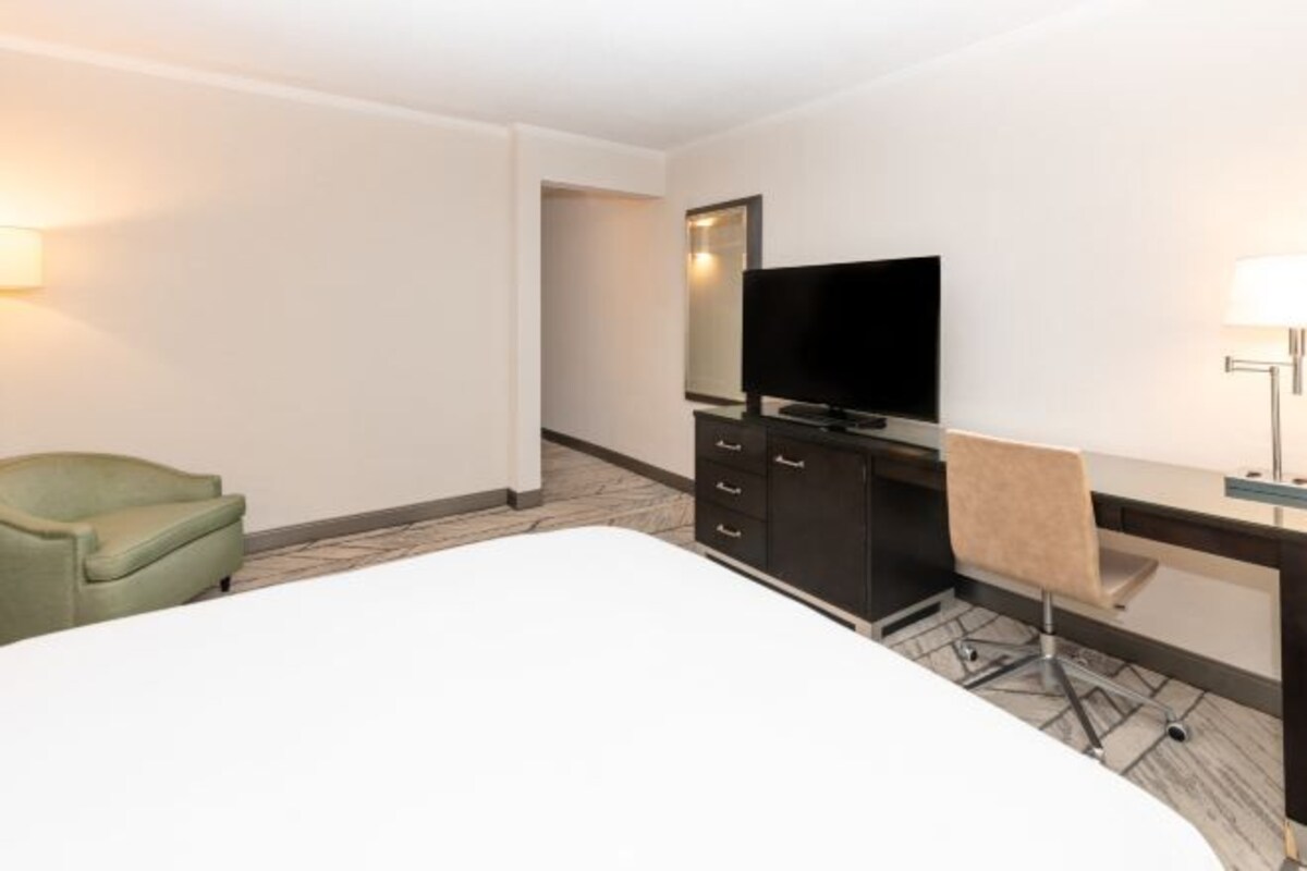 A hotel room with a bed, a desk with a chair, a television, and a wardrobe.