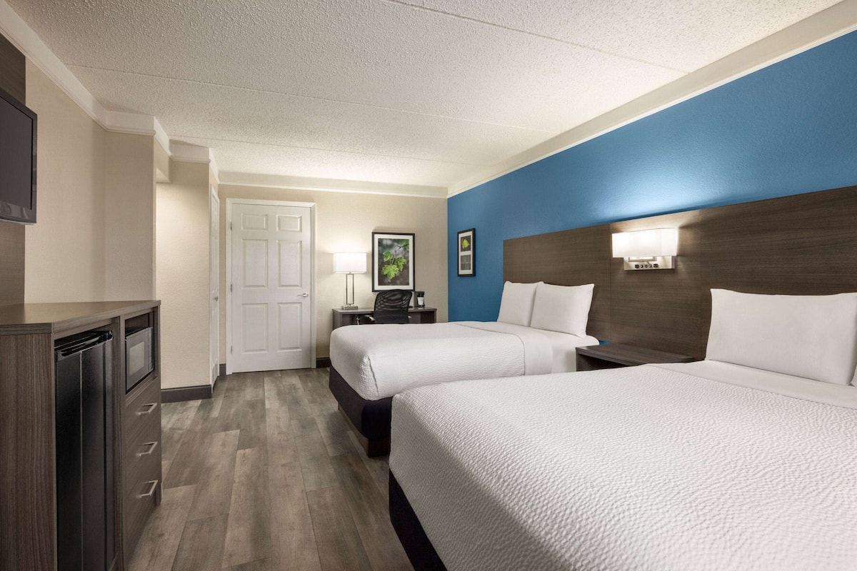 A hotel room with two beds, a desk, a lamp, and a television.