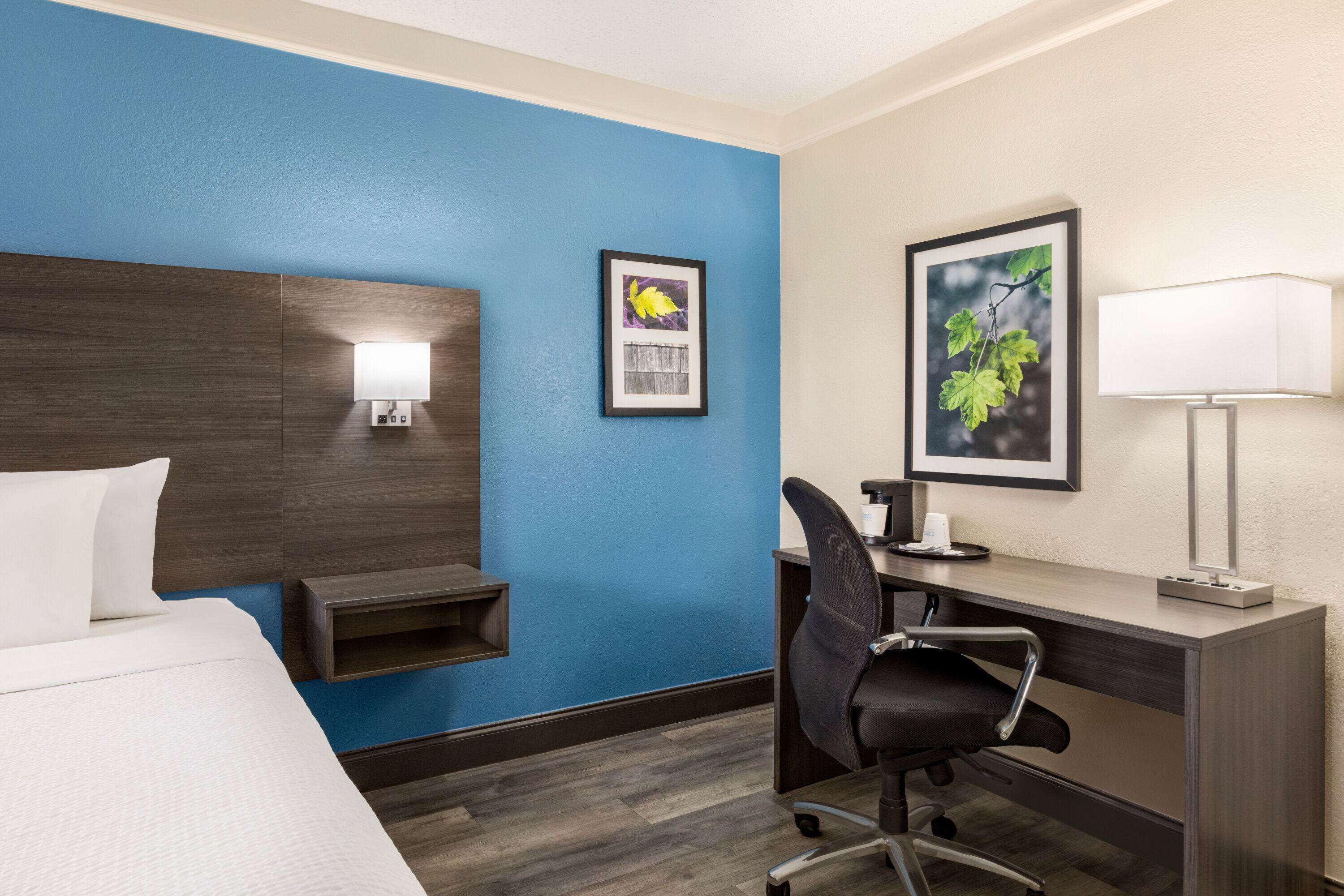 Une chambre d’hôtel avec un lit, un bureau, une chaise et deux tableaux encadrés au mur.