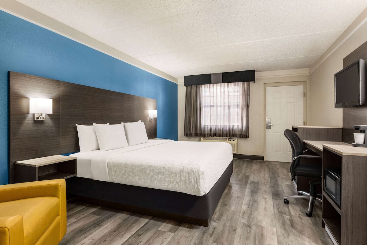 A hotel room with a large bed, a desk, a chair, a TV, and a window with curtains.