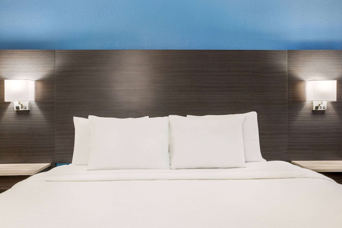 A hotel room with a large bed, two bedside lamps, and a dark wood headboard.