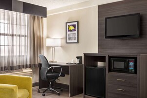 Habitación de hotel con escritorio, silla, televisión, microondas y un refrigerador pequeño.