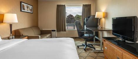 Una habitación de hotel con una cama grande, un escritorio con computadora, un televisor y dos lámparas.