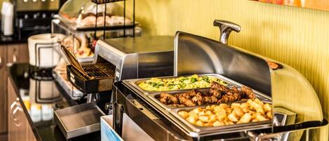 A buffet setup with various food items including meats, potatoes, and vegetables.