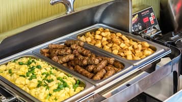 A buffet with three trays of food: scrambled eggs, sausages, and roasted potatoes.