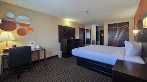 A hotel room with a large bed, a desk with a chair, a television, and a wall-mounted TV.