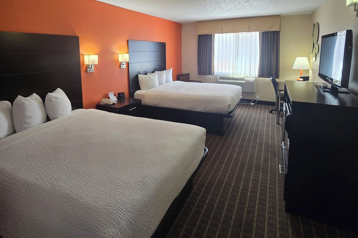 A hotel room with two beds, a desk, a television, and a window with curtains.