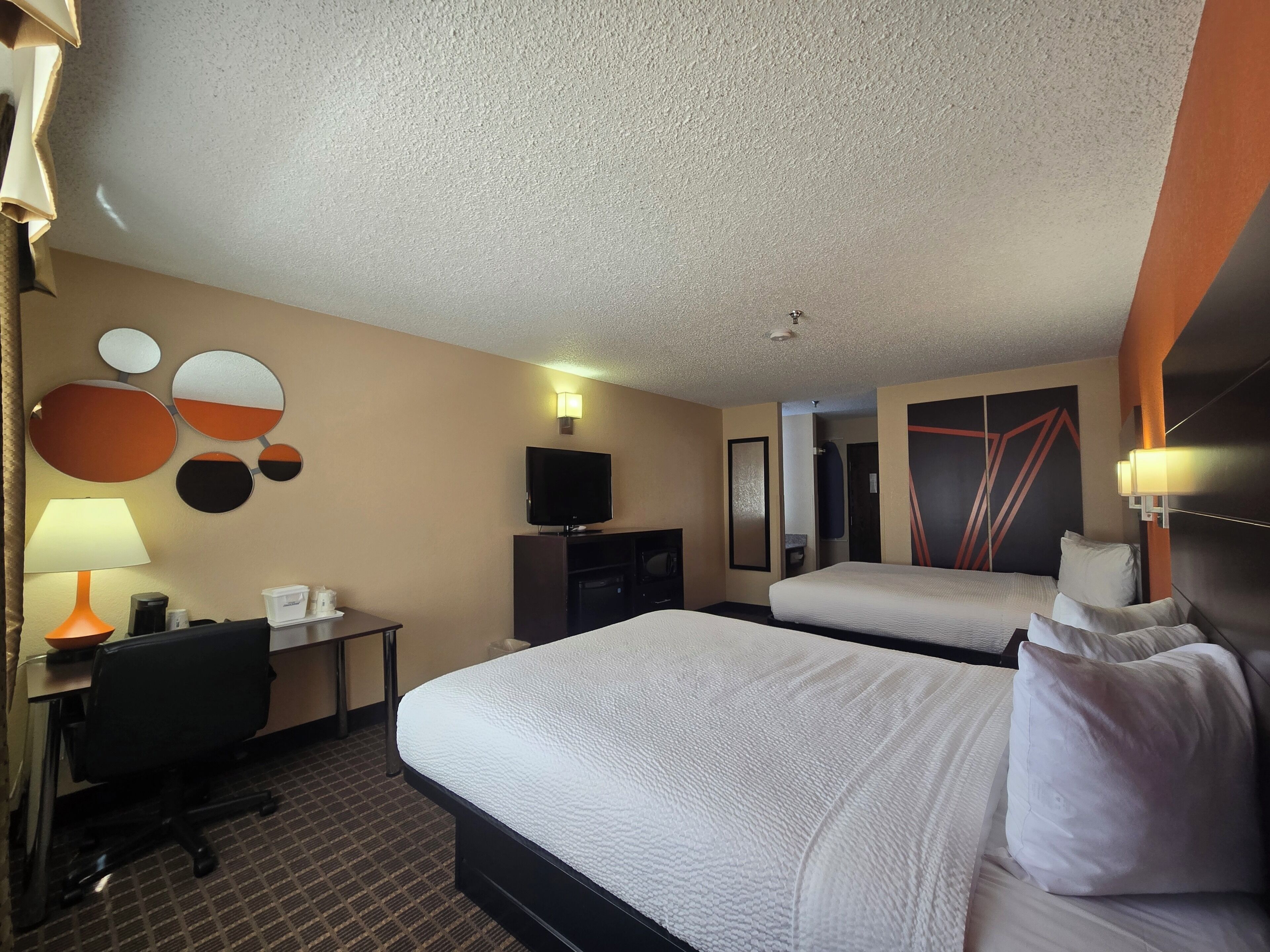 Una habitación de hotel con dos camas, un escritorio con silla, un televisor y lámparas de pared.