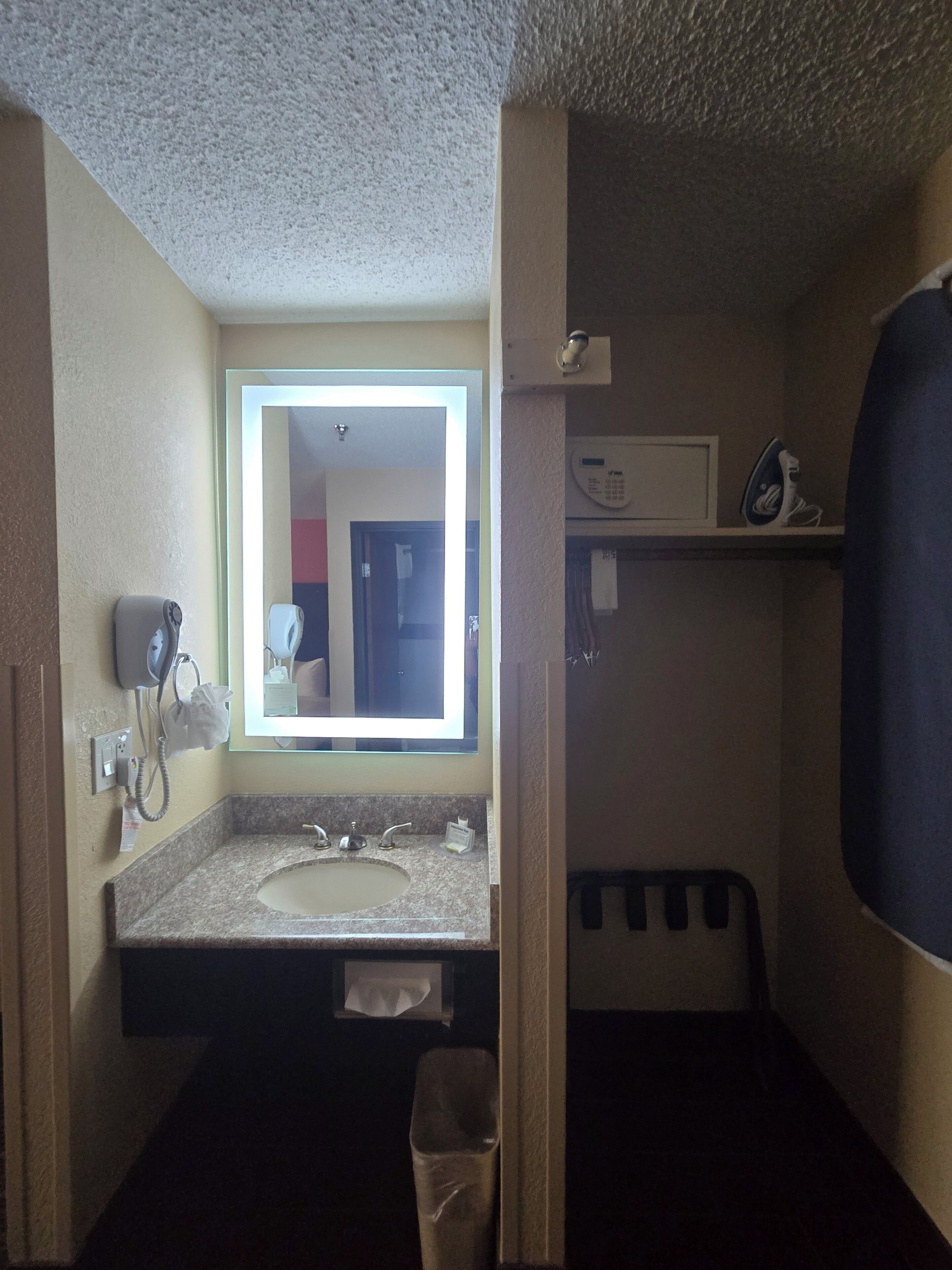 A bathroom with a sink, mirror, towel dispenser, and a shower area.