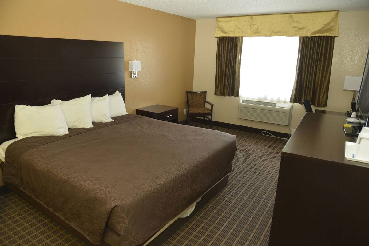 A hotel room with a large bed, a desk, a chair, a lamp, and a window with curtains.