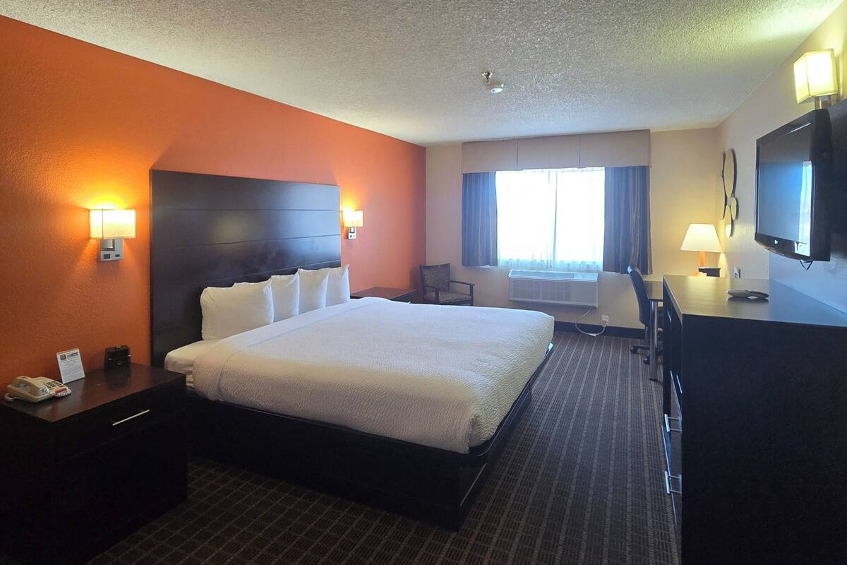 A hotel room with a large bed, a desk, a chair, a TV, and a window with curtains.