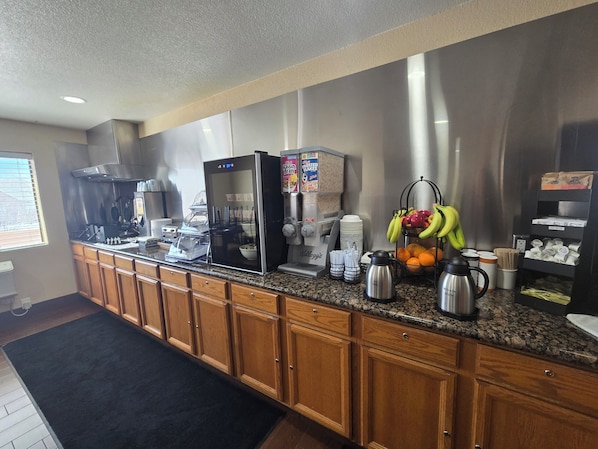 A kitchenette with a refrigerator, coffee maker, and fruit bowl.