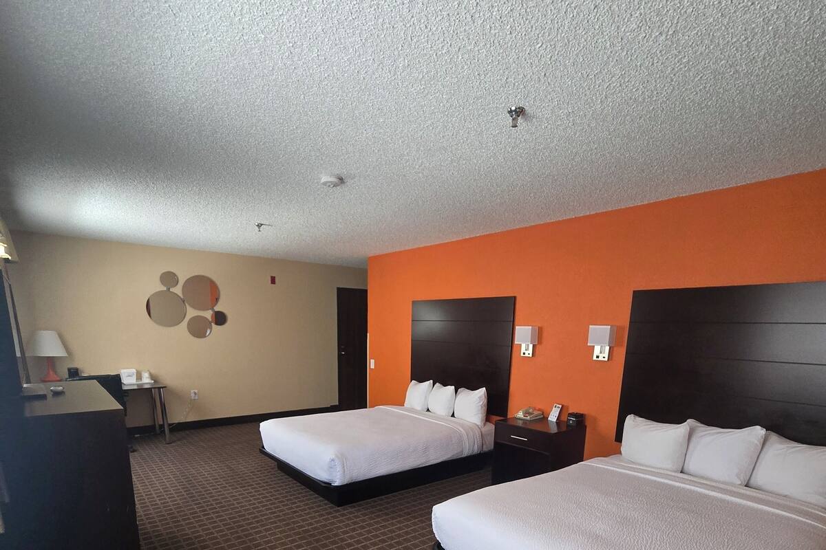 A hotel room with two beds, a desk, a lamp, and a wall-mounted mirror.