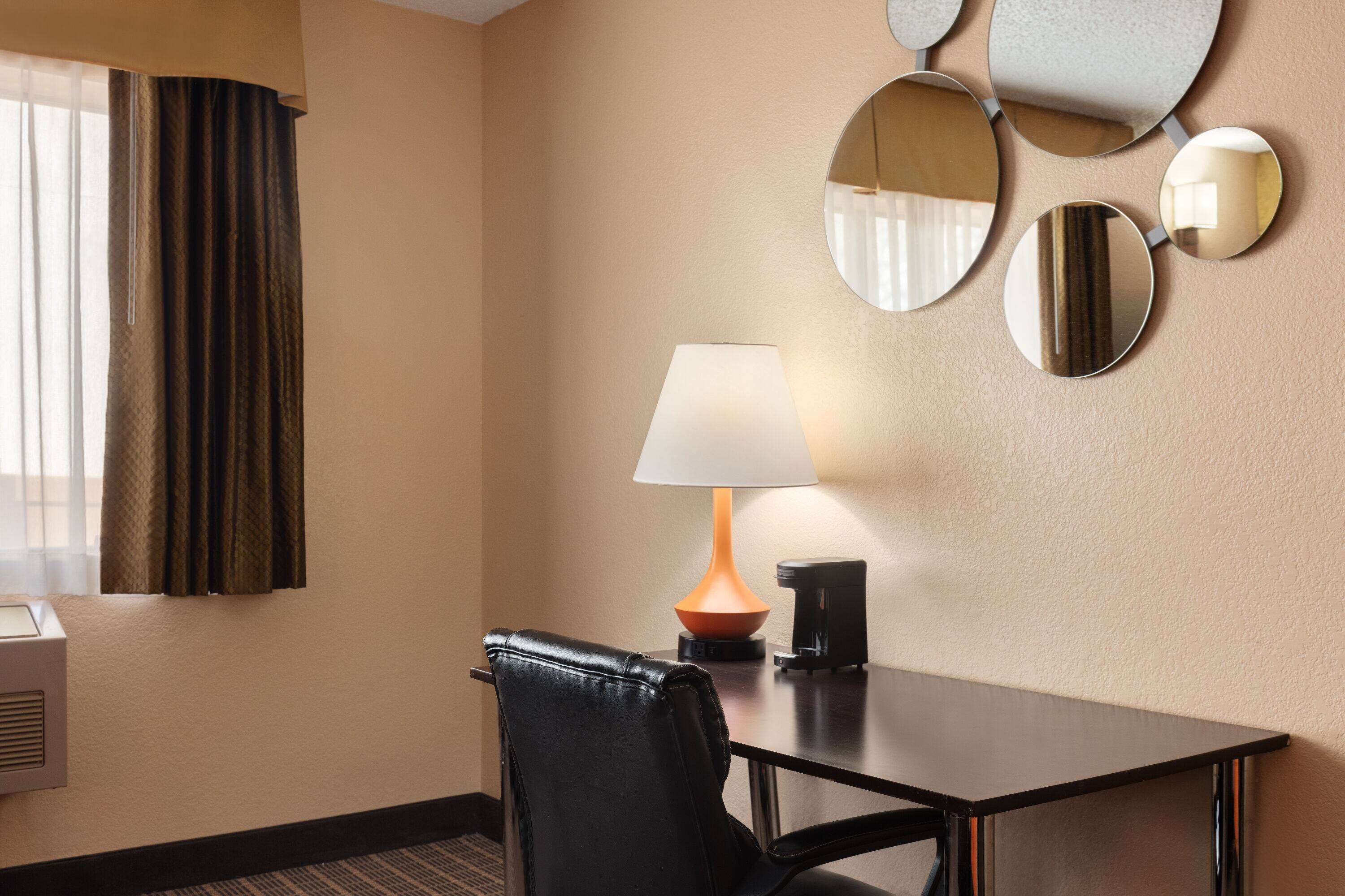 Habitación de hotel con una mesa, una silla, una lámpara y un espejo montado en la pared.