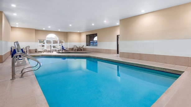 An indoor swimming pool with a clear blue water, surrounded by beige walls and a tiled floor.