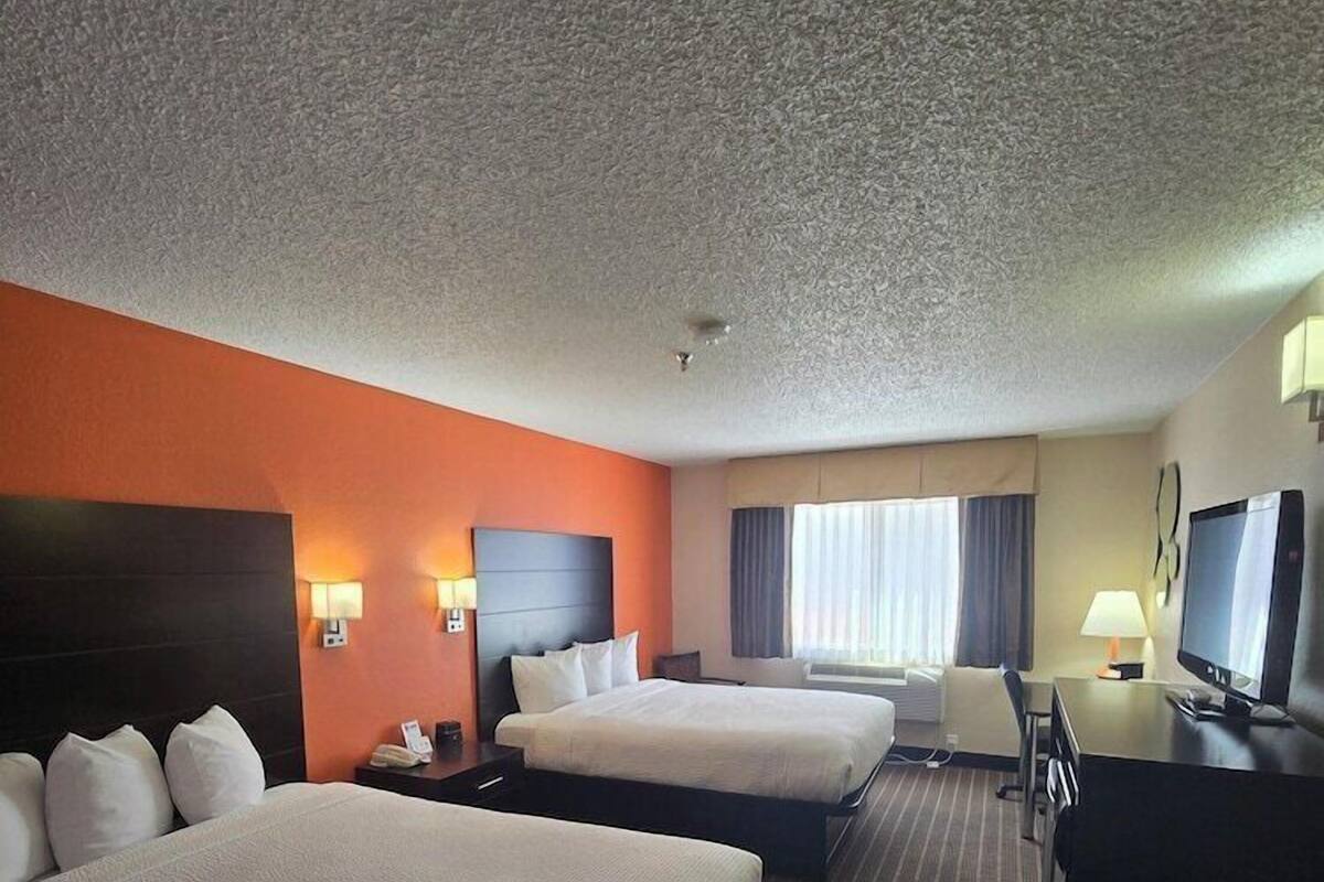 A hotel room with two beds, a desk, a television, and a window with curtains.