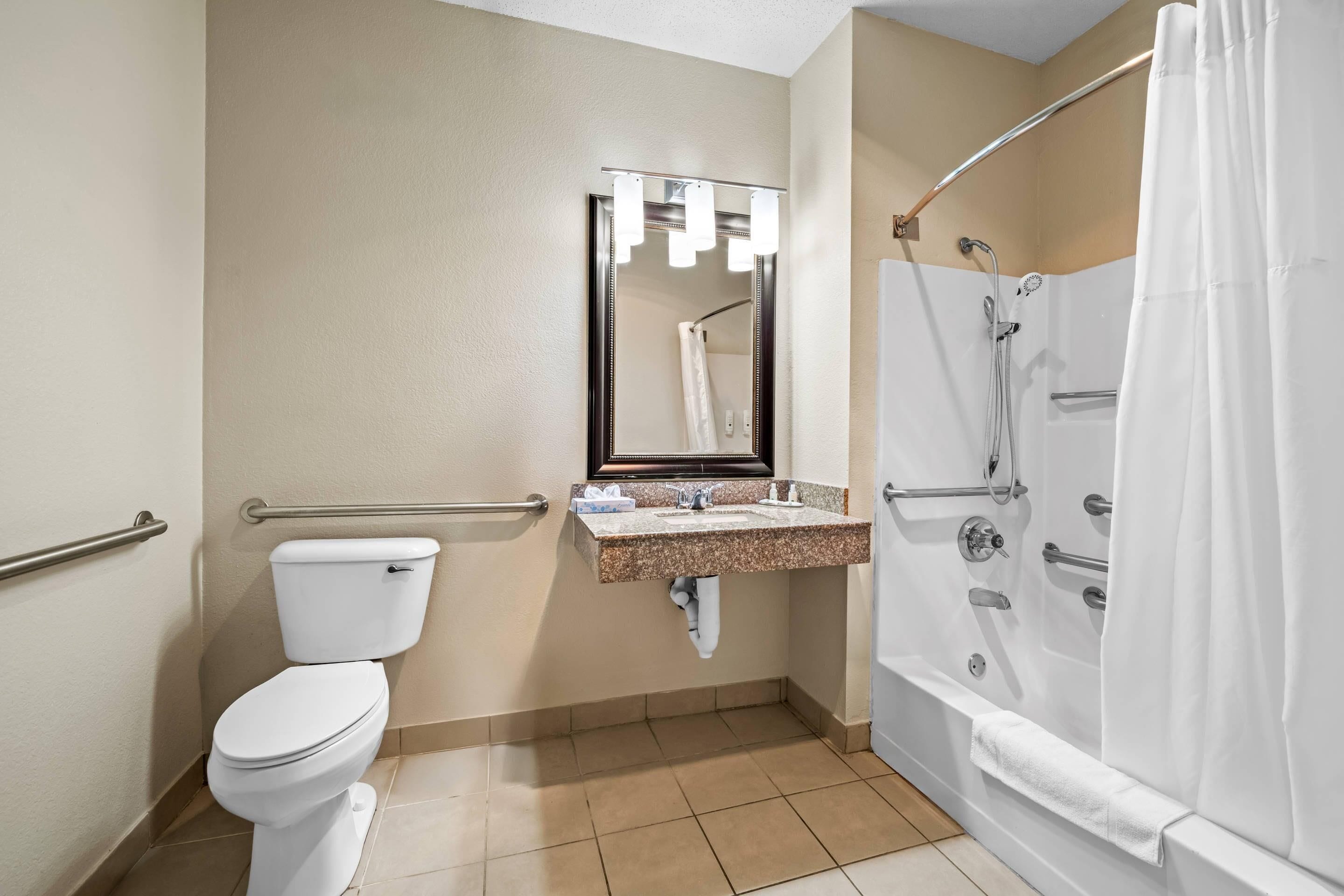 A bathroom with a toilet, sink, mirror, and shower.