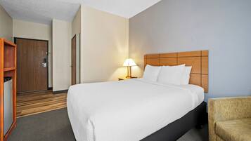 Une chambre d’hôtel avec un grand lit, une tête de lit en bois, une table de chevet avec une lampe, une armoire et un petit fauteuil.
