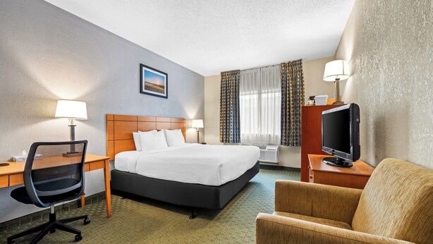 A hotel room with a bed, desk, chair, television, and curtains. - Quality Inn Dubuque on Hwy 20 (Dubuque)