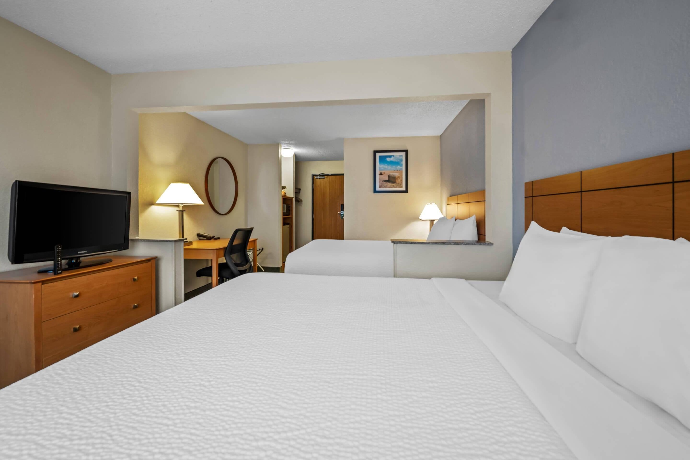 A hotel room with a large bed, a desk, a television, and two lamps.