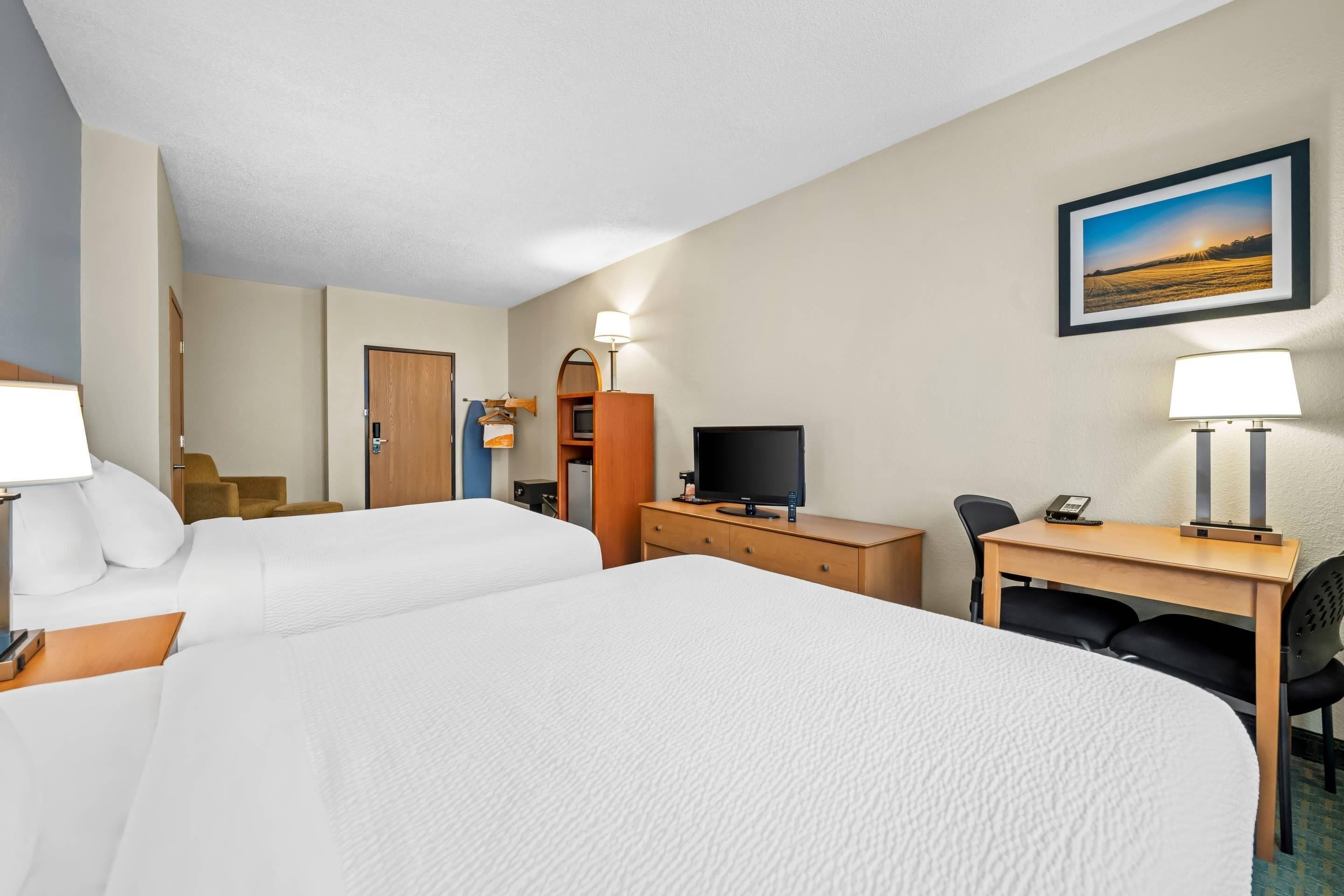 A hotel room with two beds, a desk, a television, and a desk lamp.