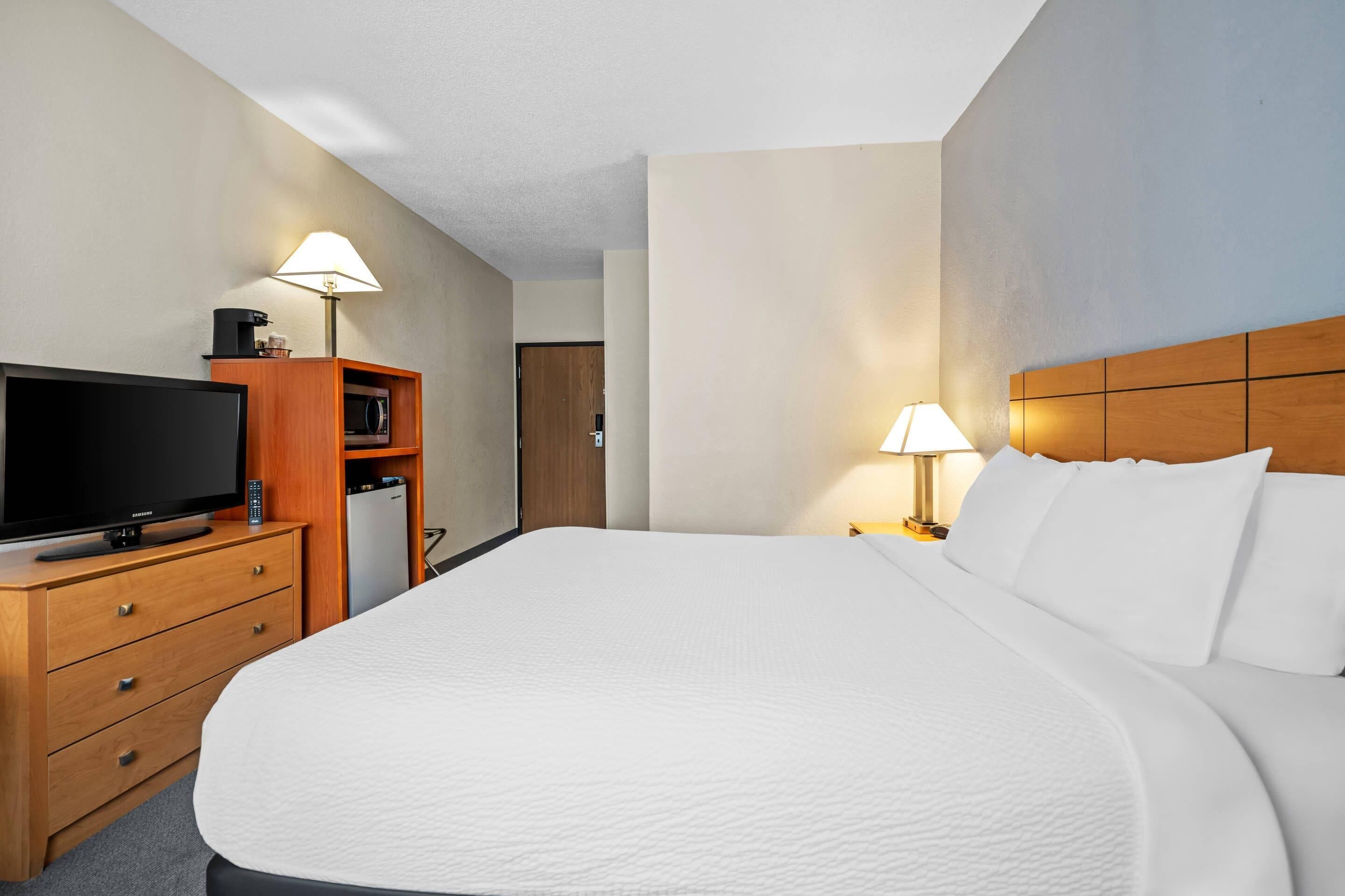 Een hotelkamer met een groot bed, een televisie op een houten dressoir, een magnetron en een lampje op het nachtkastje.
