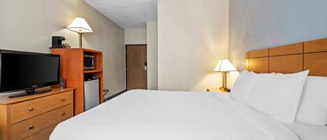Een hotelkamer met een groot bed, een televisie op een houten dressoir, een magnetron en een lampje op het nachtkastje.