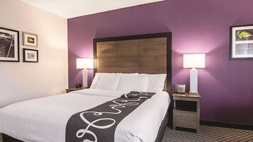 Habitación de hotel con una cama grande, dos mesitas de noche, un cabecero y una pared de acento morada.