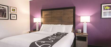 Habitación de hotel con una cama grande, dos mesitas de noche, un cabecero y una pared de acento morada.