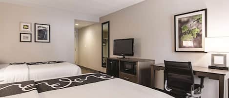 A hotel room with two beds, a desk, a chair, a television, and framed pictures on the wall.