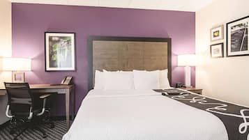 Habitación de hotel con una cama grande, un escritorio y una silla. Hay dos lámparas de noche y un cuadro en la pared.