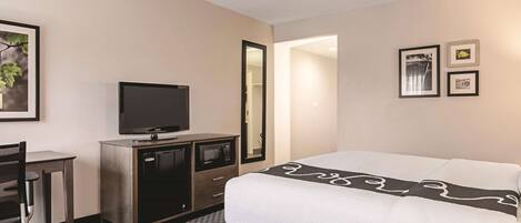 A hotel room with a bed, a desk with a television, a microwave, and a mirror.