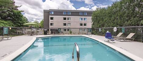 A swimming pool with a metal ladder, lounge chairs, and a building in the background.