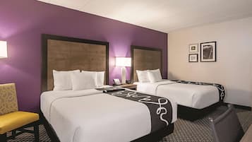 A hotel room with two beds, a desk, a chair, and a lamp.
